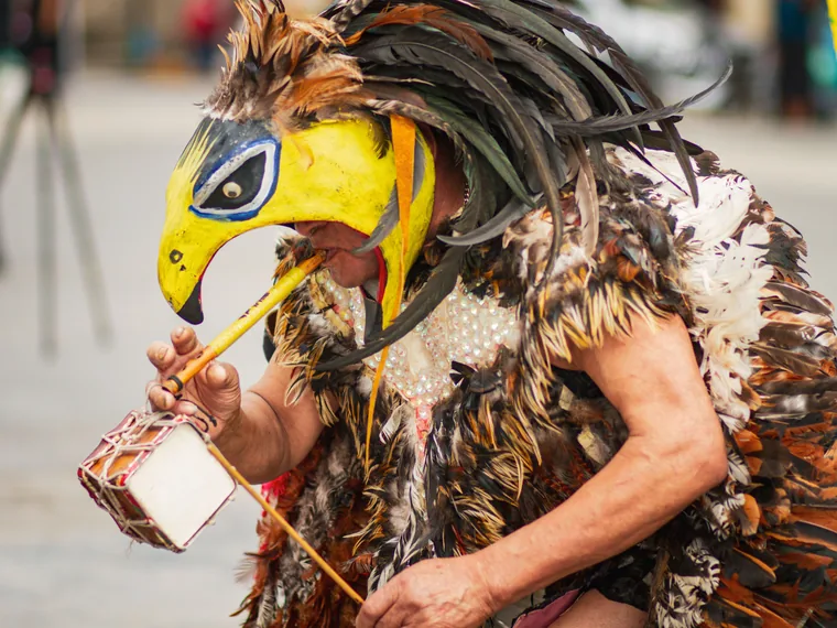 Danzante tradicional con tocado de plumas tocando un tambor ceremonial, representando el respeto por los rituales ancestrales